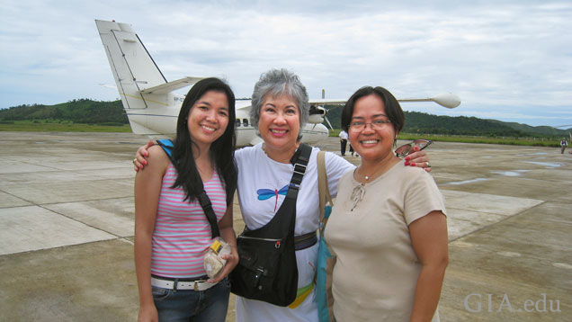 Three woman stand on a runway with a plane in the background.